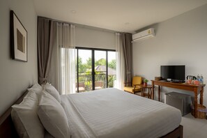 A hotel room with a large bed, a desk with a TV, a small fridge, and a view of greenery outside. - Ploen Pirom (Bangkok)