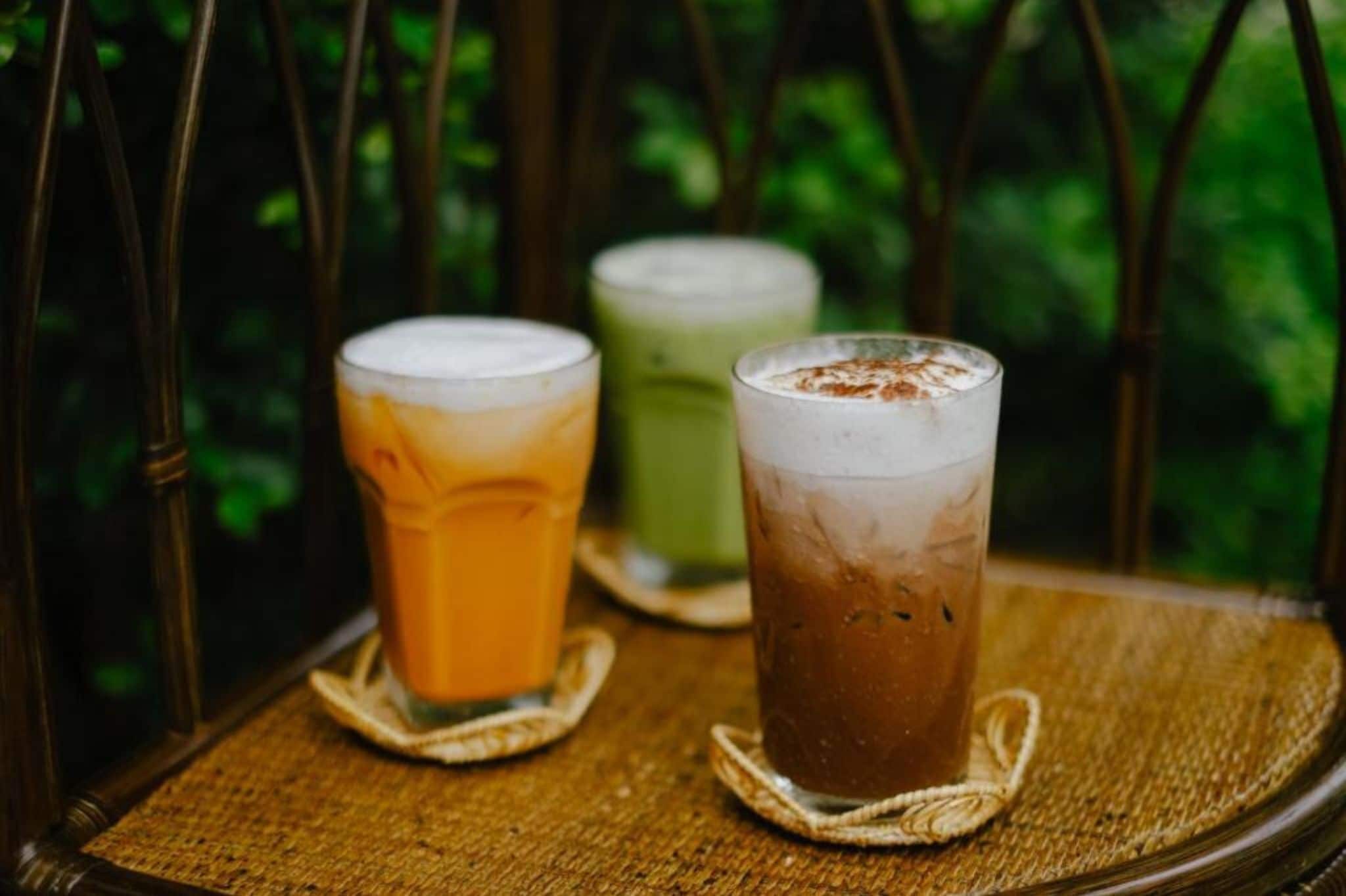 Trois verres de boissons glacées posés sur un tapis en fibres naturelles, le tout mis en valeur par un décor de verdure.