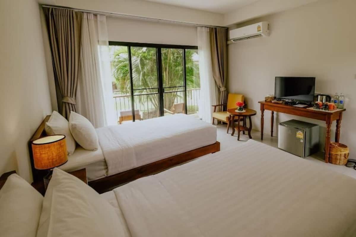 A hotel room with two beds, a TV, a small desk, and a view of palm trees.