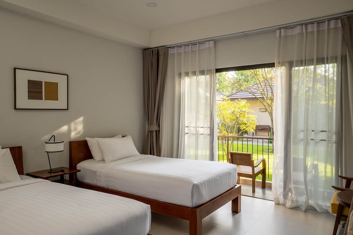 A hotel room with two beds, a nightstand, a lamp, and a balcony with a chair.