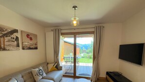 Un salon comprenant un canapé, une table basse, un téléviseur et une porte-fenêtre coulissante donnant sur un espace extérieur.