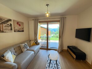 A living room with a sofa, a coffee table, a TV, and a sliding glass door leading to an outdoor area. - New apartment 6 ppl Les Saisies, terrace, parking (Hauteluce)