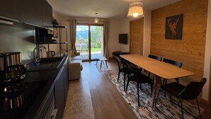 Une cuisine moderne dotée d’une cuisinière intégrée, un coin repas avec une table et des chaises en bois, et une grande porte-fenêtre coulissante donnant sur un balcon.