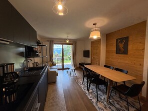 A modern kitchen with a built-in stove, a dining area with a wooden table and chairs, and a large sliding glass door leading to a balcony. - New apartment 6 ppl Les Saisies, terrace, parking (Hauteluce)