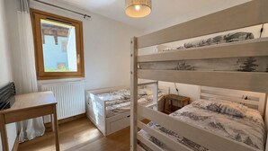 Une chambre avec des lits superposés, un bureau, un radiateur et une fenêtre avec des rideaux.