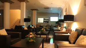 Un vestíbulo de hotel con sofás de cuero, una mesa de centro con flores, una escalera y una zona de bar.