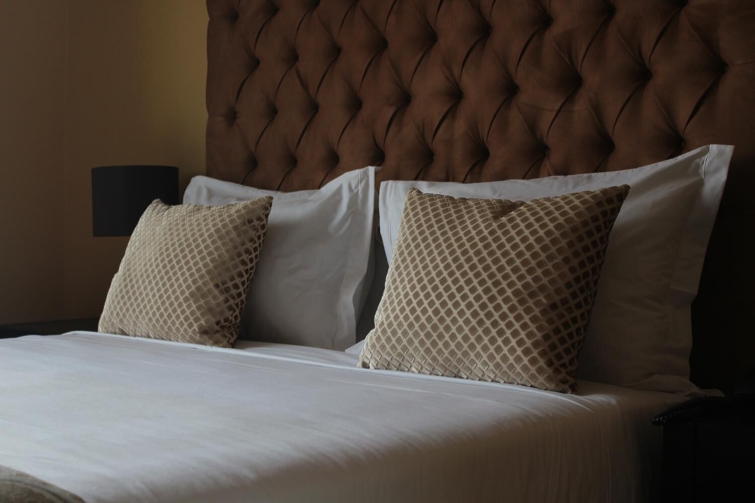 A bed with a tufted headboard, two patterned pillows, and a white bedspread.