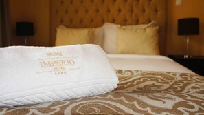 Una cama de hotel con una toalla blanca que dice "IMPERIO HOTEL" y una colcha estampada.