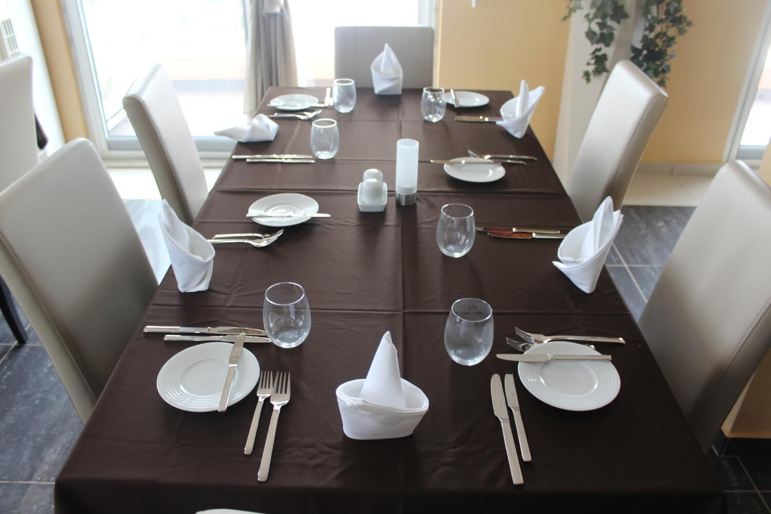 A dining table set for four with white plates, cutlery, and glasses, surrounded by white chairs.