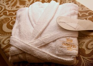 Bata blanca doblada con el letrero 'IMPERIO HOTEL' bordado, sobre una tela estampada.