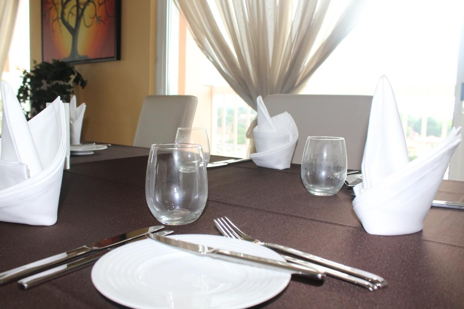 Une table à manger dressée pour quatre personnes, avec des serviettes blanches, des verres transparents et des couverts.