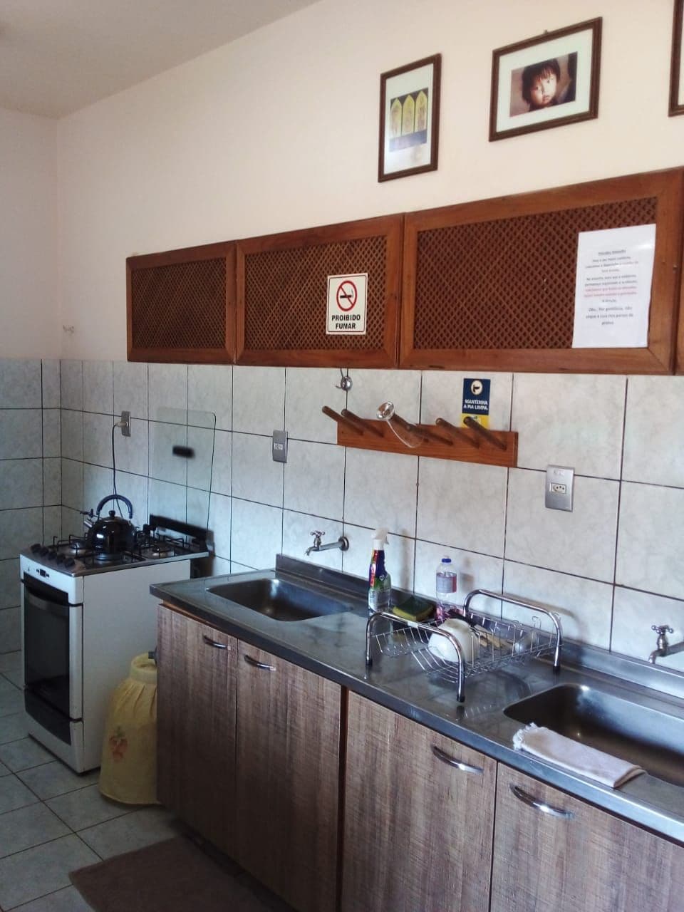 A kitchen with a stove, sink, and wooden cabinets. There are two framed pictures on the wall and a sign prohibiting smoking.