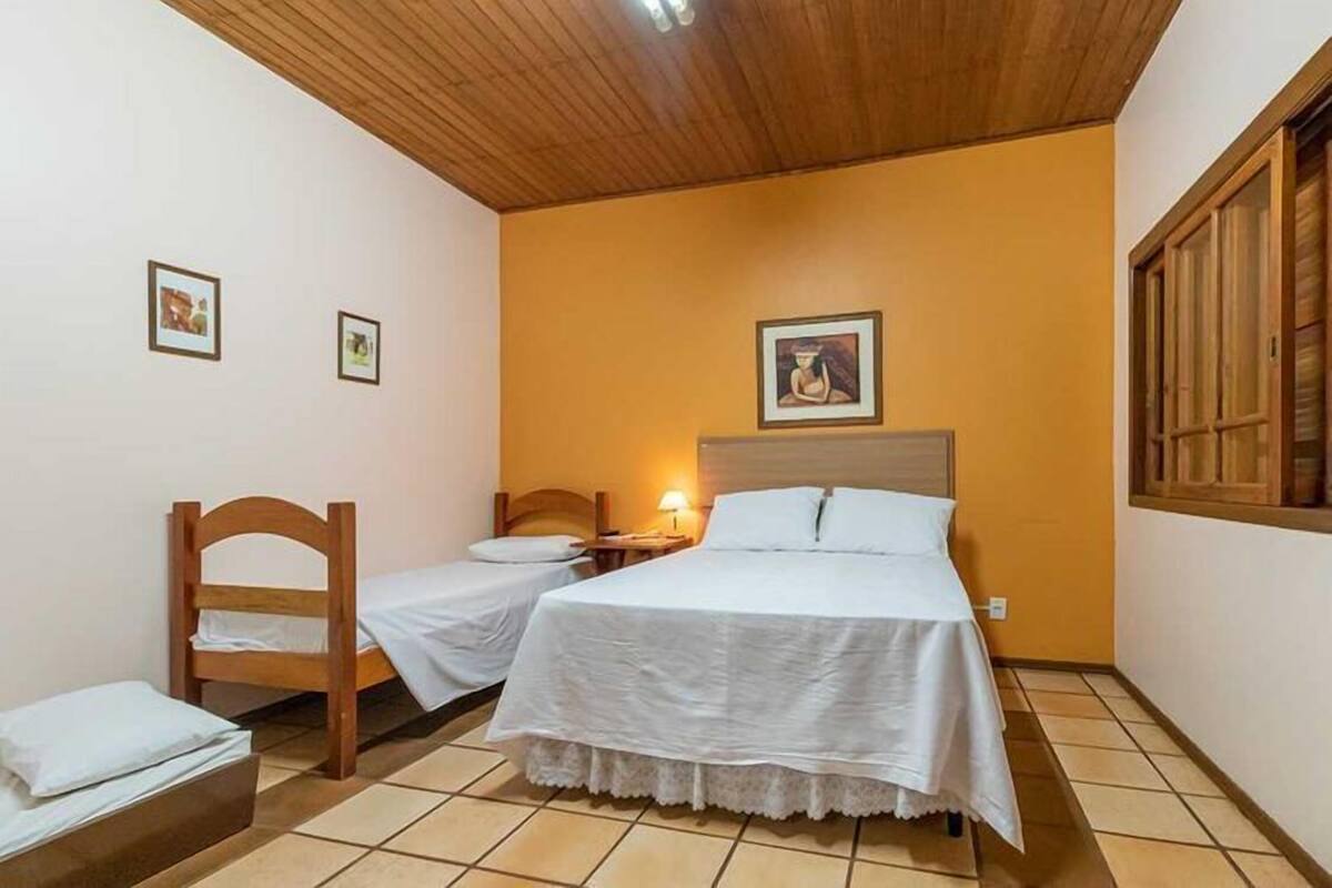 A room with two single beds, a wooden chair, a small table with a lamp, and a picture on the wall.