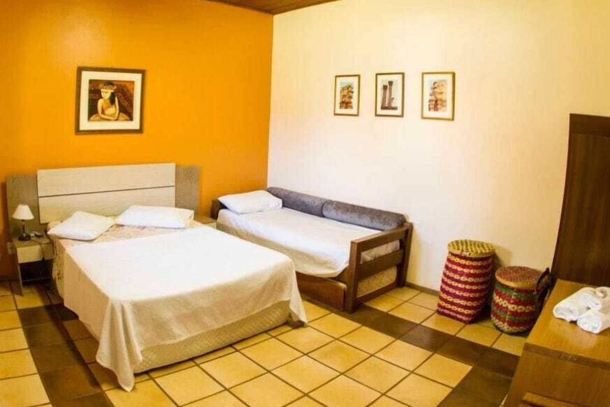 A room with two beds, a wooden headboard, a tiled floor, and a wall with three framed pictures.