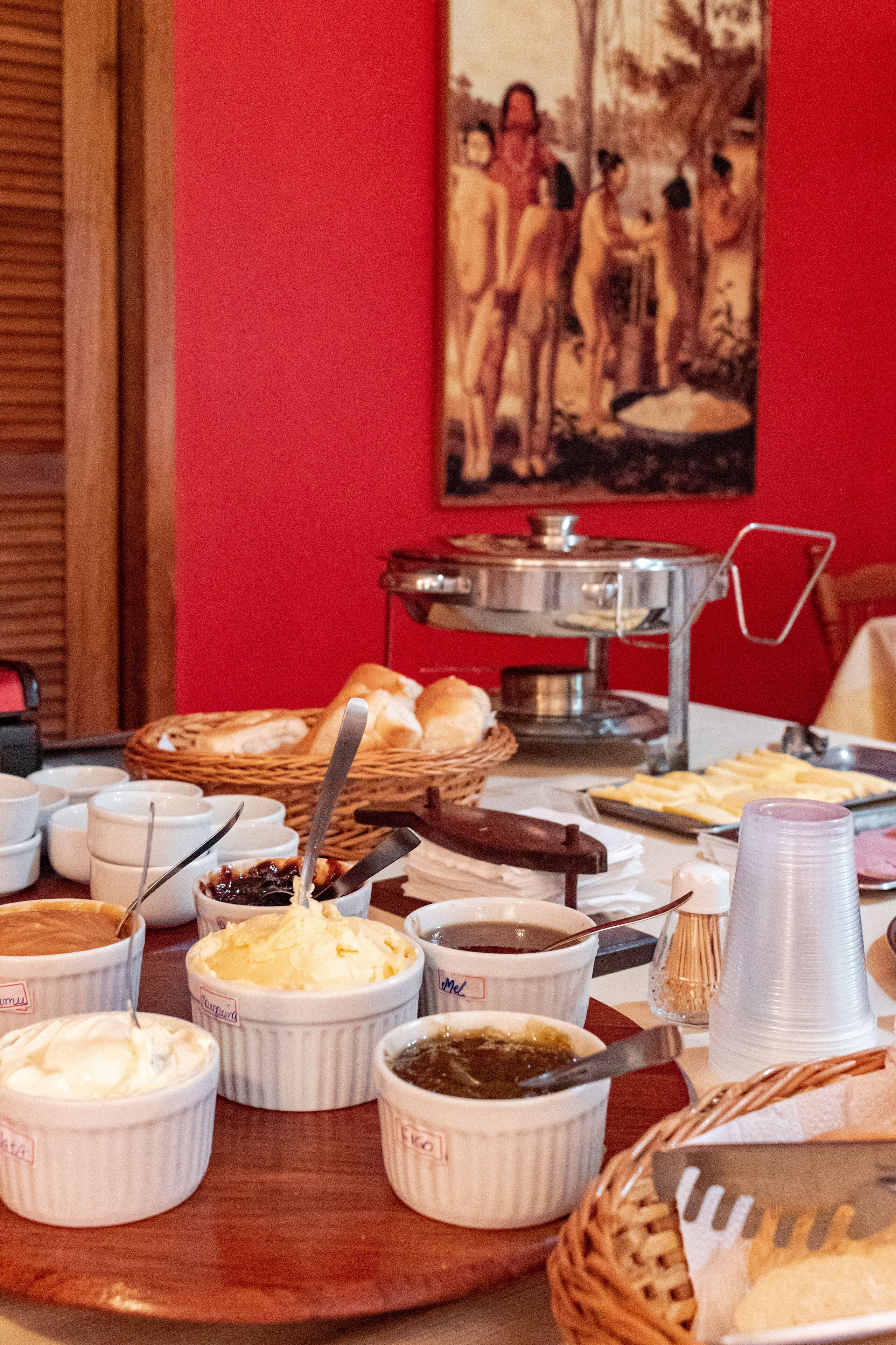 Uma mesa de buffet com diversos alimentos e acompanhamentos, uma cesta de pão e um salver de prata.