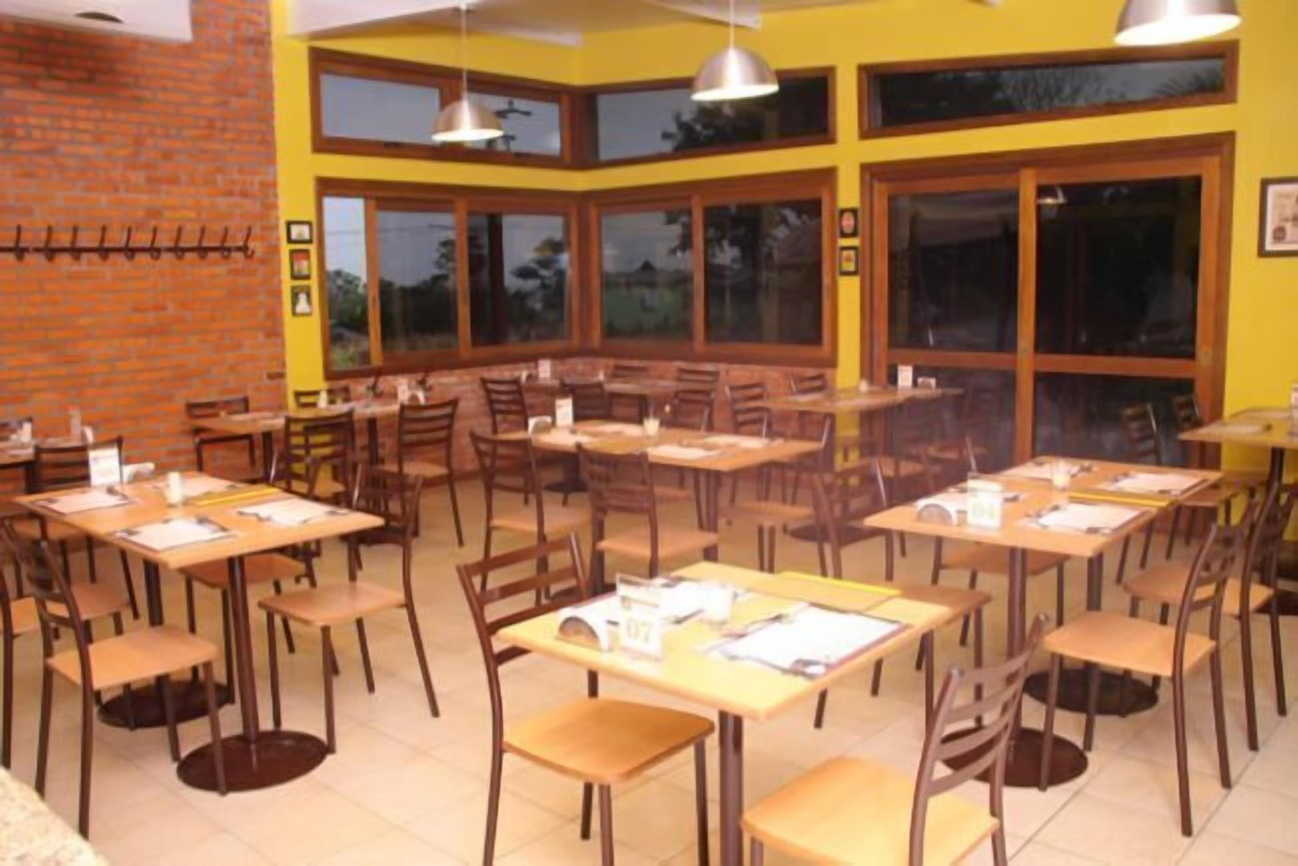 A restaurant with multiple tables and chairs, large windows, and a brick wall.