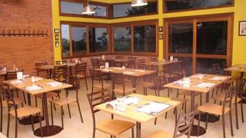 A restaurant with multiple tables and chairs, large windows, and a brick wall.