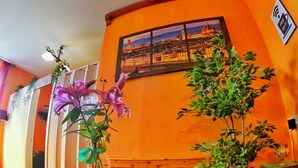Une pièce avec une table en bois recouverte d’une nappe à motifs, un vase rempli de fleurs roses et une plante en pot.