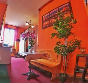 A room with a wooden bench, a table with a vase of flowers, a potted plant, and a painting on the wall. - Holiday Rooms Florence (Florence)