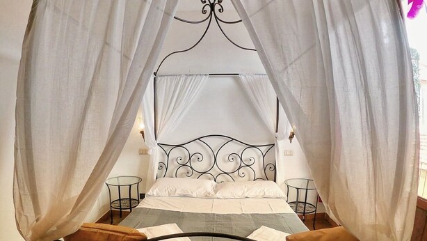 Un lit à baldaquin à quatre poteaux, avec une tête de lit en métal, une literie blanche et deux tables de chevet avec des lampes.