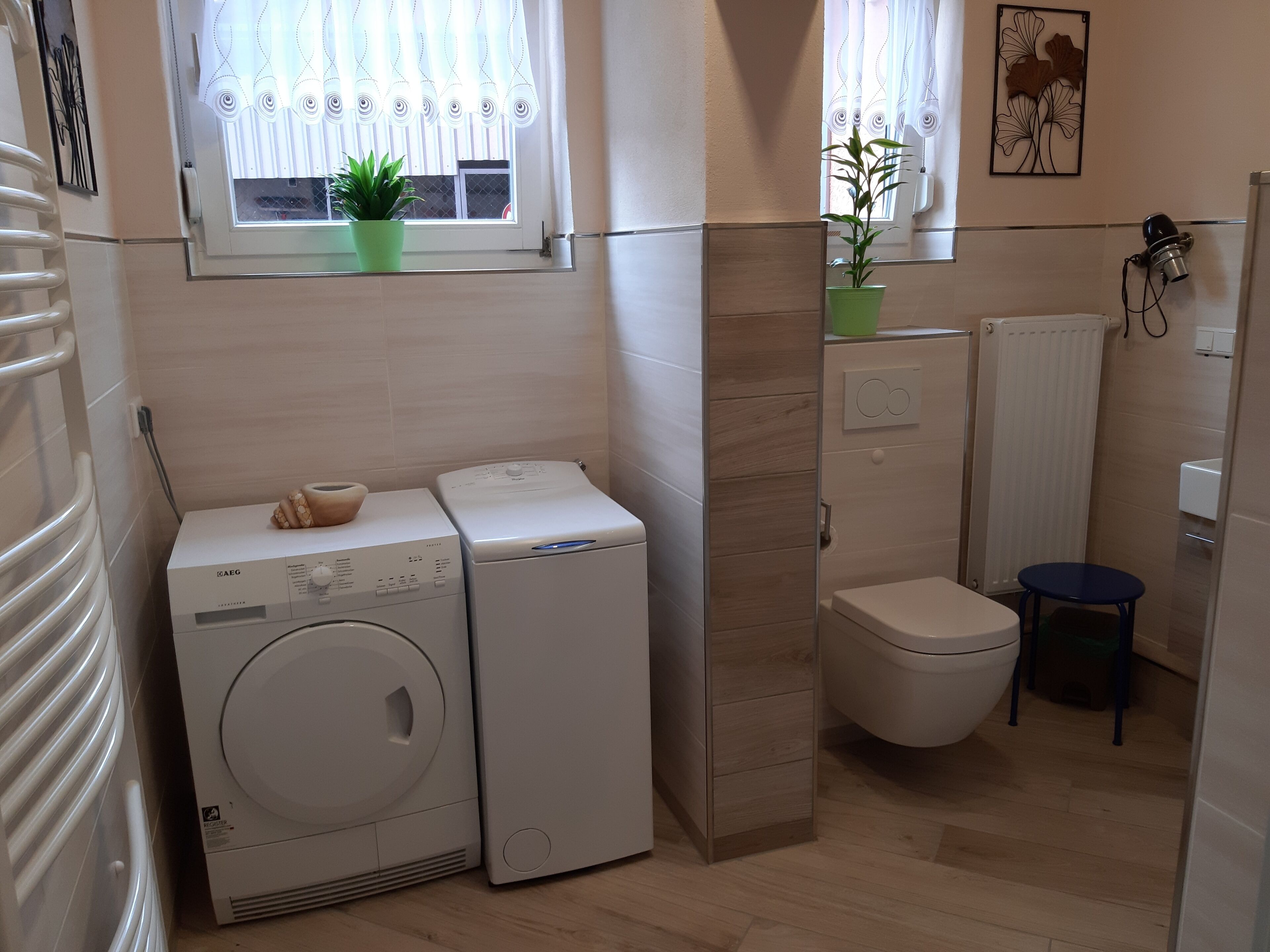 A compact laundry room with two stacked washing machines, a toilet, and a radiator.