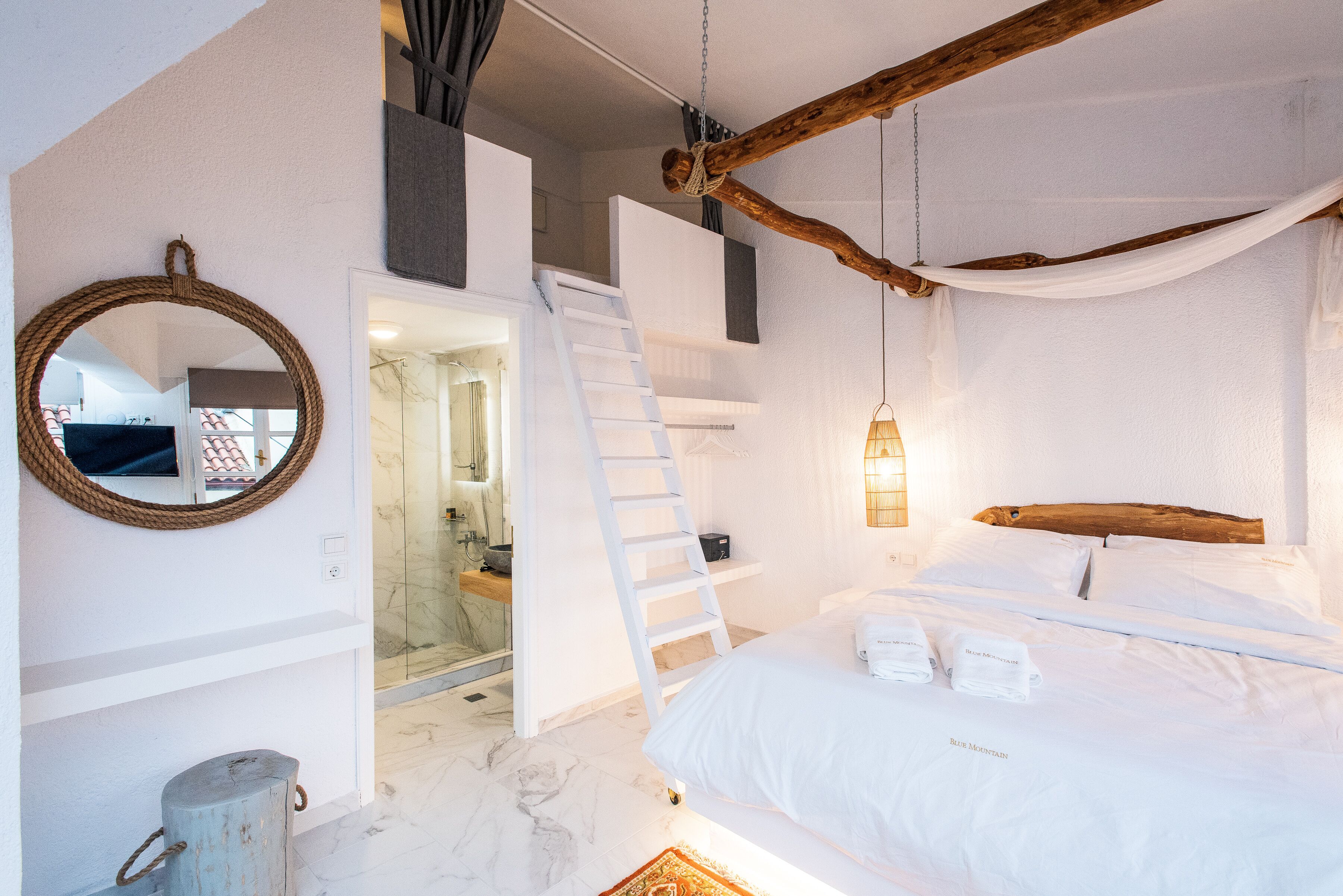 A bedroom with a bed, a wooden headboard, a ladder, a hanging light fixture, and a mirror on the wall.