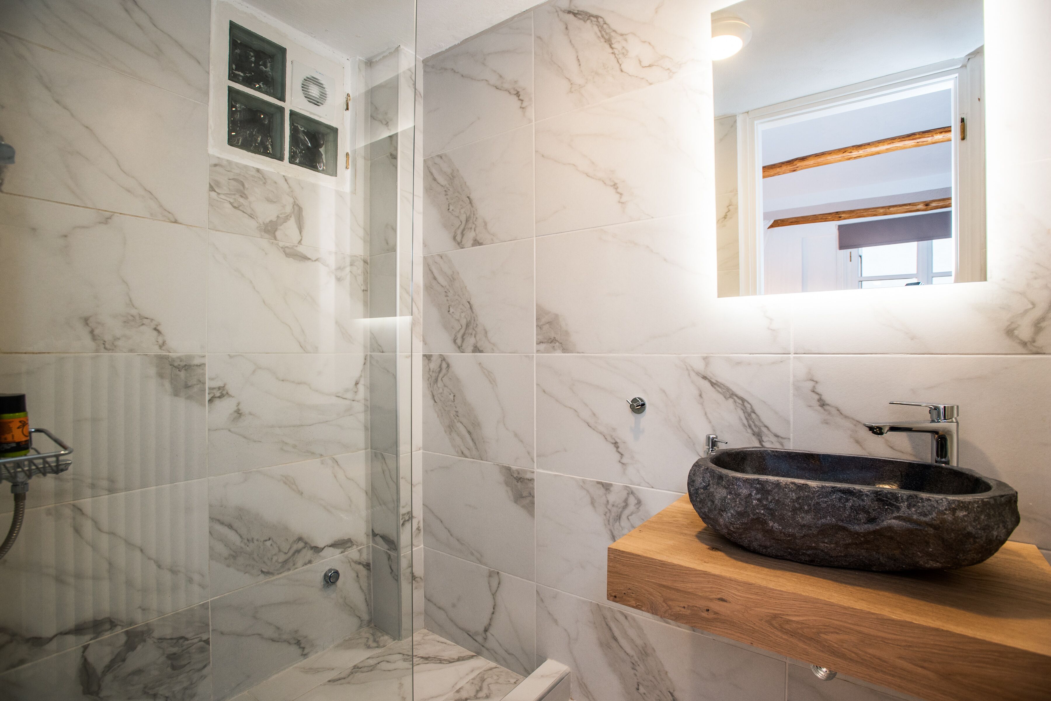 A bathroom with marble tiles, a stone sink, and a glass shower enclosure.