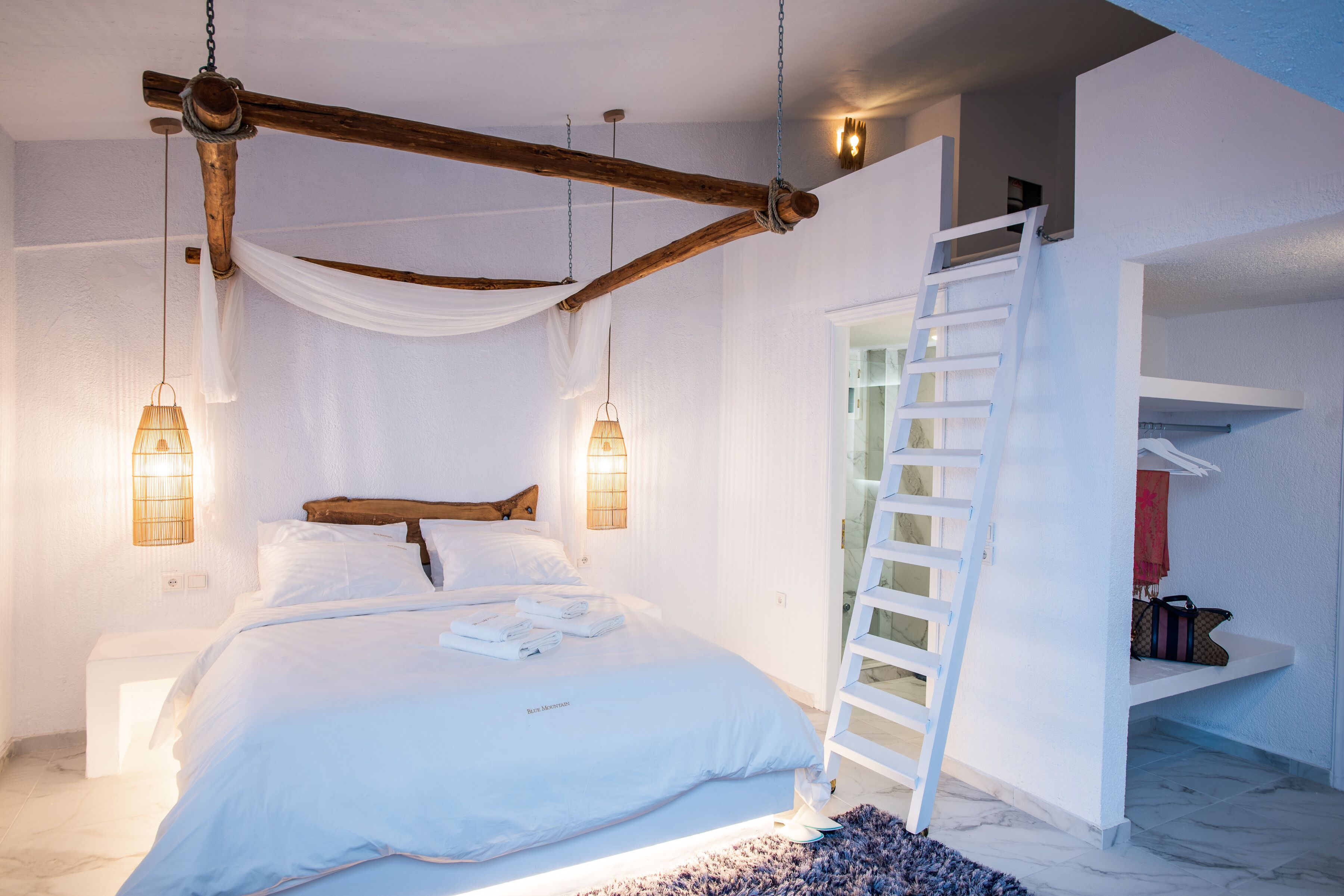 A bedroom with a bed, bedside lamps, a wooden ladder, and a white bench.