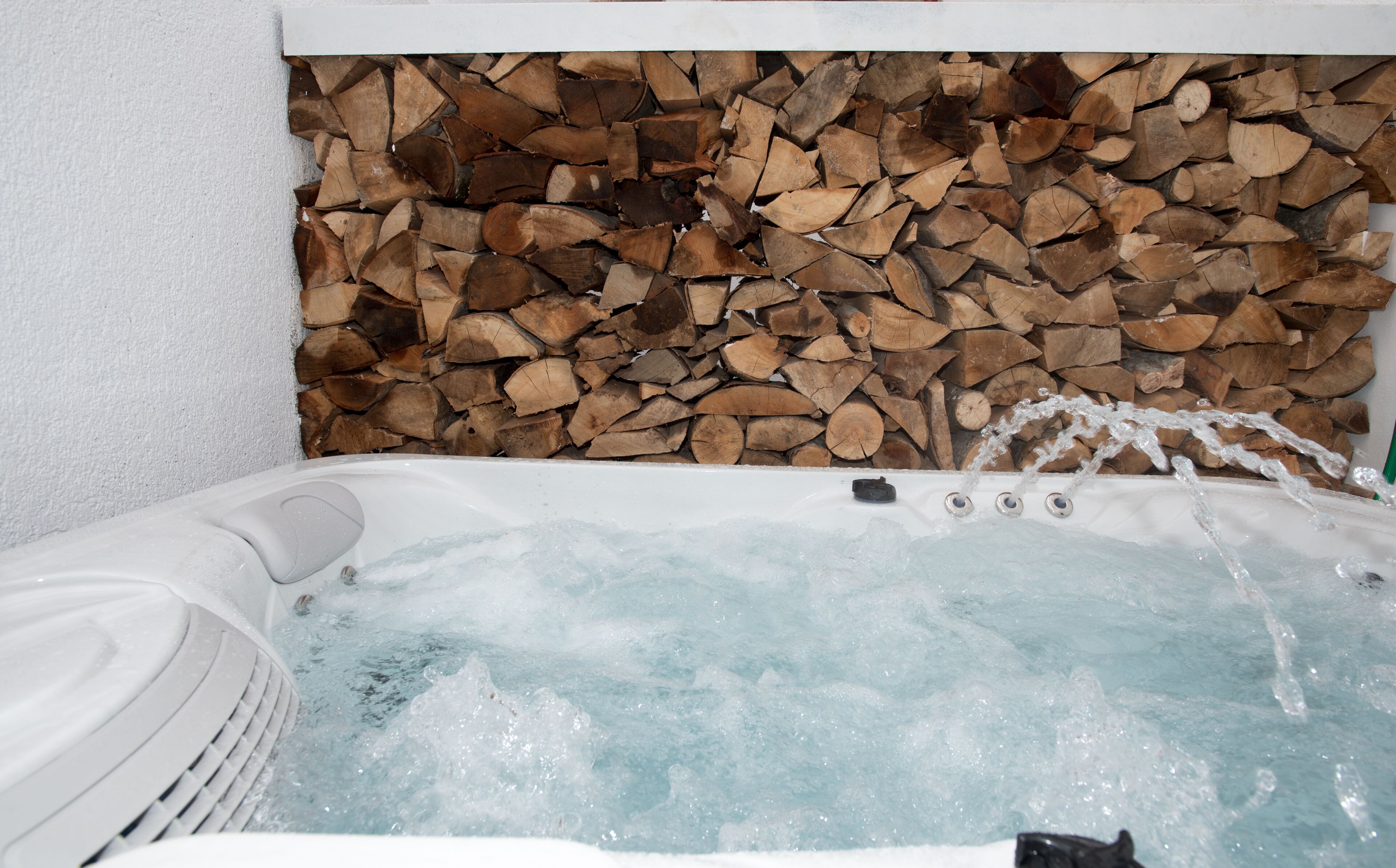 A hot tub with water running, surrounded by a wall of stacked firewood.