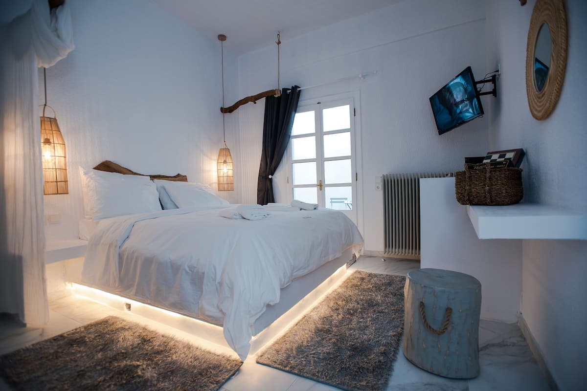 A modern bedroom with a large bed, bedside lamps, a mounted TV, and a view of the outdoors.