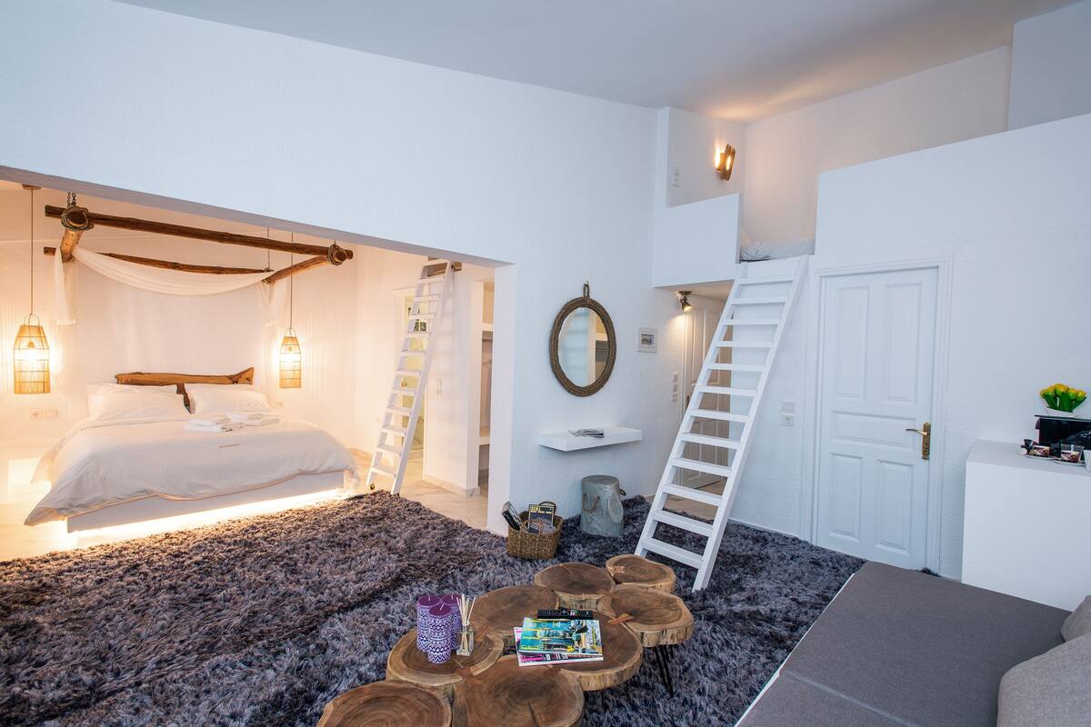 A bedroom with a bed, bedside lamps, a wooden coffee table, a ladder, and a white door.