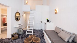 Habitación pequeña y luminosa con literas, un escritorio, un sofá y una escalera que lleva a una puerta.