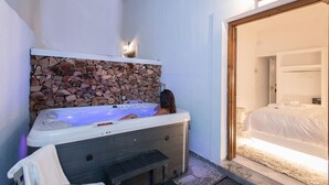 Un baño con pared de piedra, una bañera y una puerta visible que da a un dormitorio.