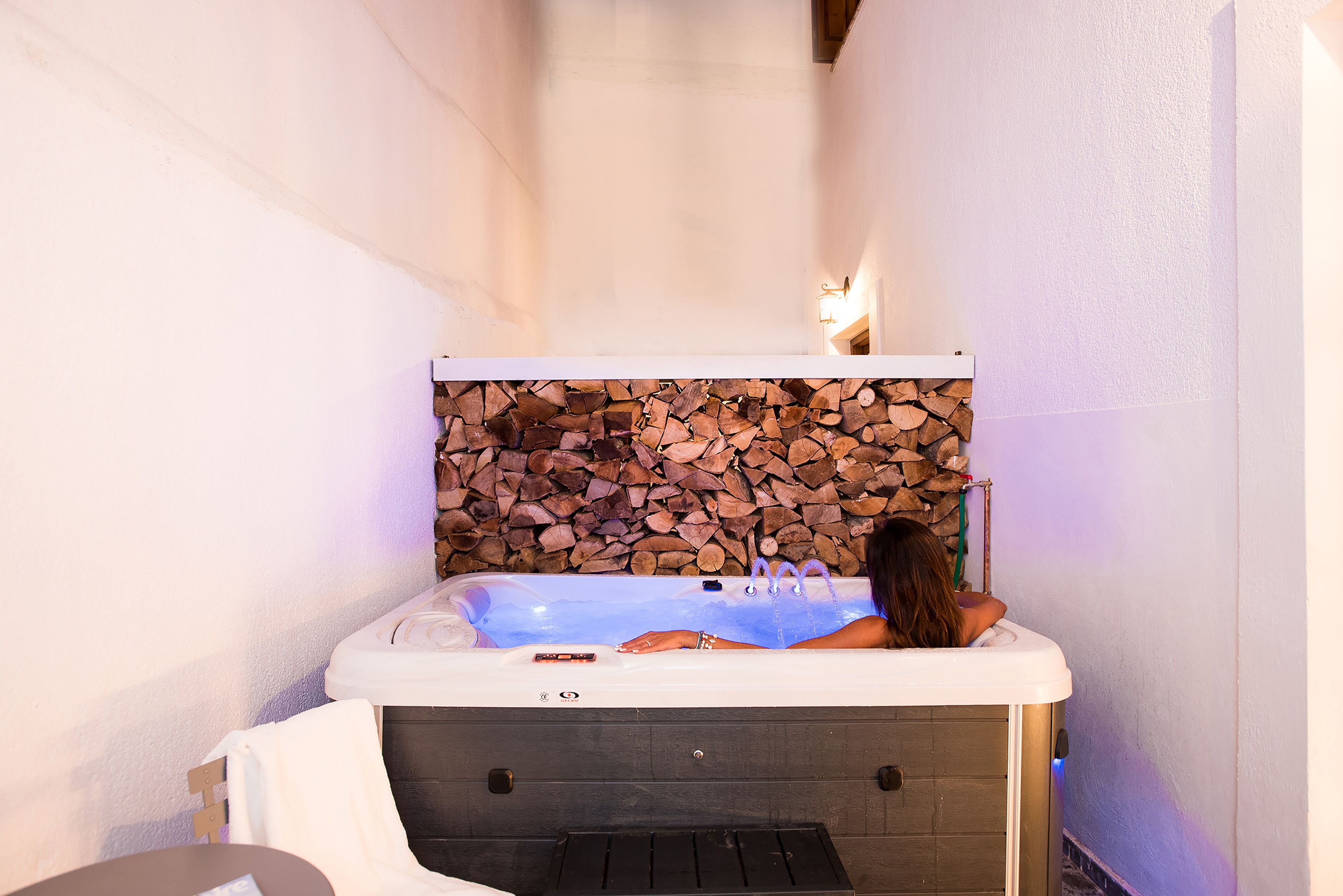 A spa area with a hot tub, a stone wall, and a wooden log backdrop.