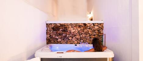 A spa area with a hot tub, a stone wall, and a wooden log backdrop.