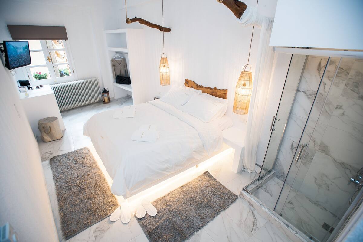 A modern bedroom with a large bed, bedside lamps, a walk-in shower, and a TV on the wall.