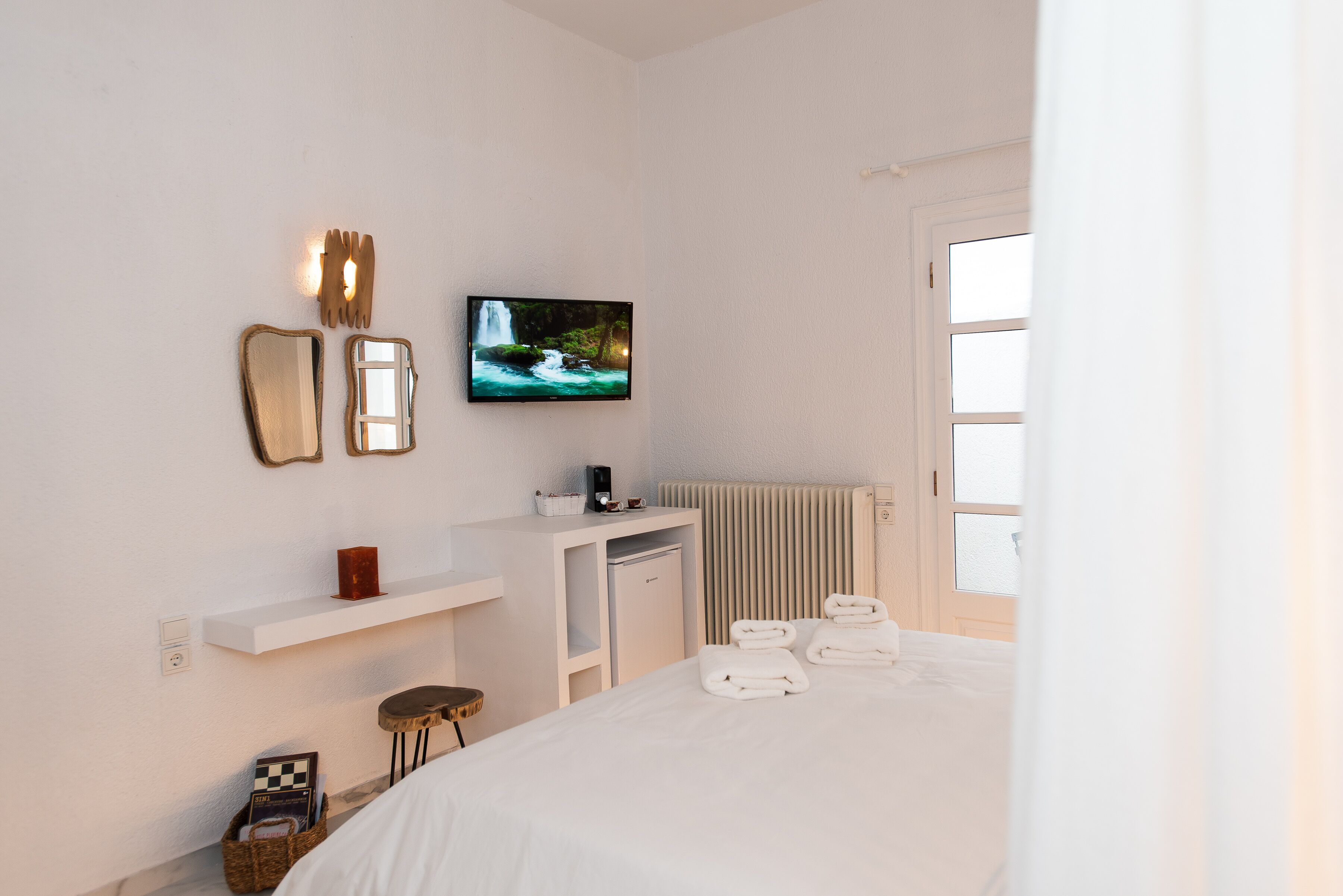 A hotel room with a bed, a television, a small desk, a radiator, and a window.