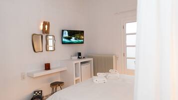 A hotel room with a bed, a television, a small desk, a radiator, and a window.
