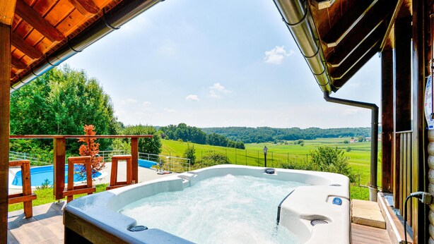 A hot tub on a patio with a view of a green landscape and a swimming pool. - Awesome home in Radakovo with sauna (Radakovo)