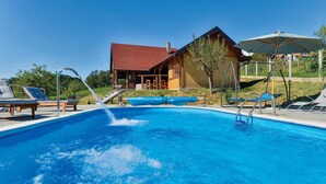A swimming pool with lounge chairs, a wooden building, and a covered area with an umbrella. - Awesome home in Radakovo with sauna (Radakovo)