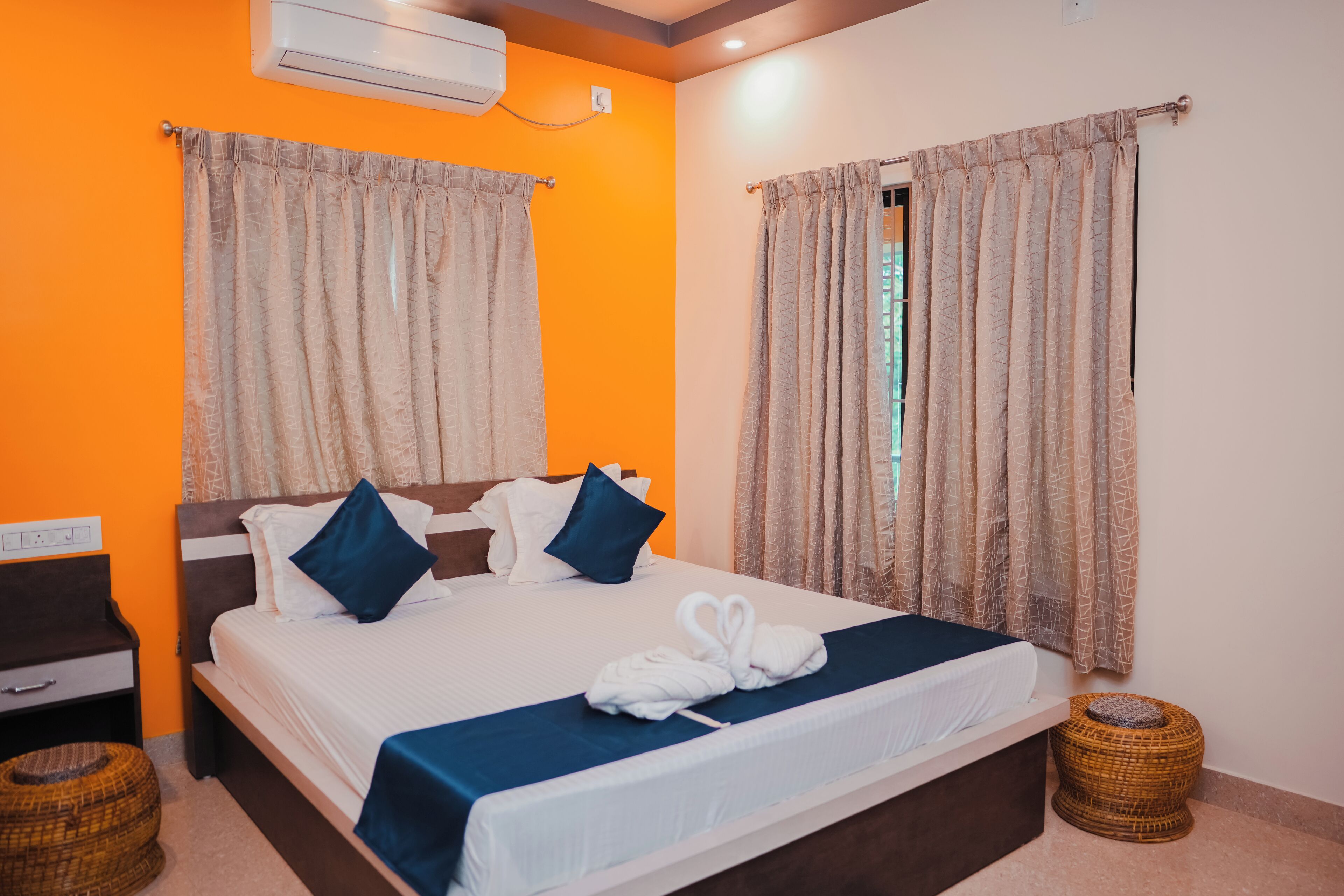 A hotel room with a bed, curtains, a nightstand, and a small wicker stool.