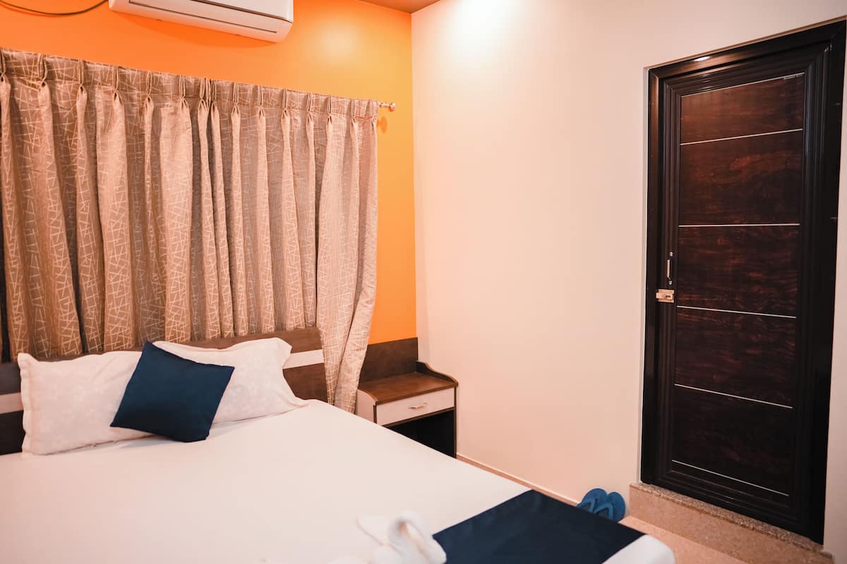 A hotel room with a bed, a nightstand, a dark wooden door, and a curtain with a geometric pattern.