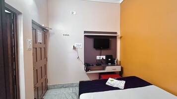 A hotel room with a bed, a desk with a computer, a TV mounted on the wall, and a door.