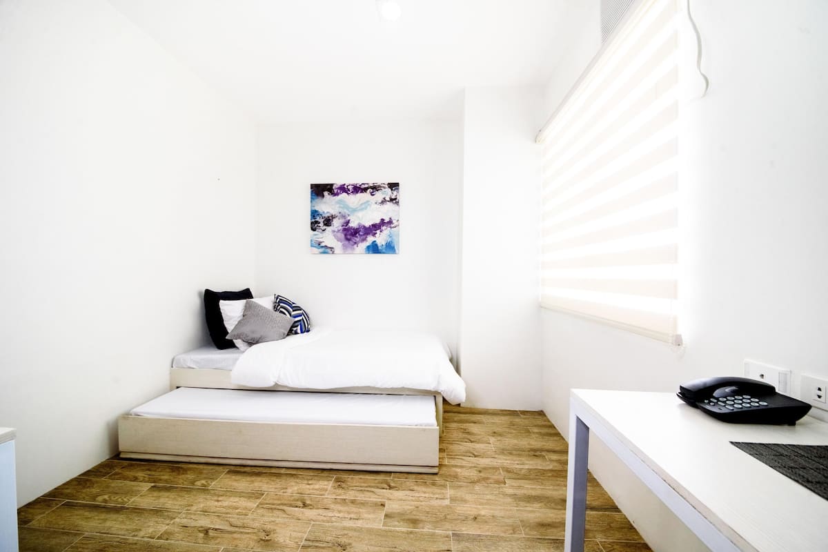A small, bright room with a bed, a desk, and a window.