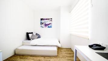 Una habitación pequeña y luminosa con una cama, un escritorio y una ventana.