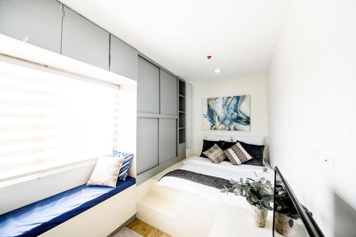A bedroom with a bed, built-in wardrobe, a window seat, and a painting on the wall.