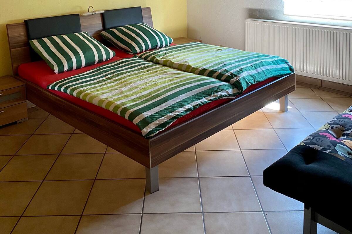 A bedroom with a bed, a nightstand, a window, a radiator, and a ceiling fan.