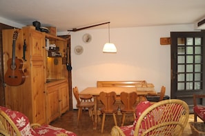 A wooden dining area with a table and chairs, a guitar, and a hanging light fixture. - JOIVY Courmayeur Entrelevie Casa di Montagna (Courmayeur)