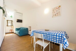 A room with a dining table, chairs, a sofa, a television, and a wall-mounted air conditioner.