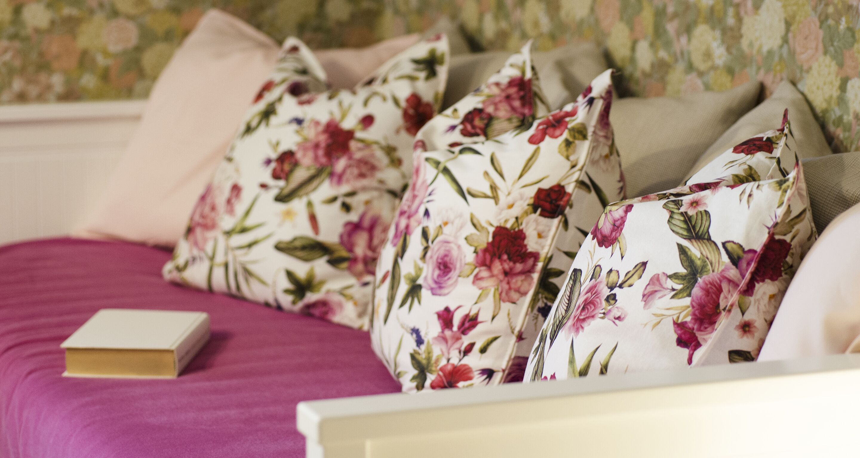 A bed with floral-patterned pillows and a book on a pink bedspread.